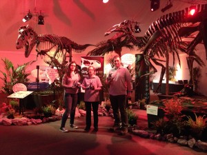 Picture of three researchers holding lego robot triceratops under two dinosaur skeletons.